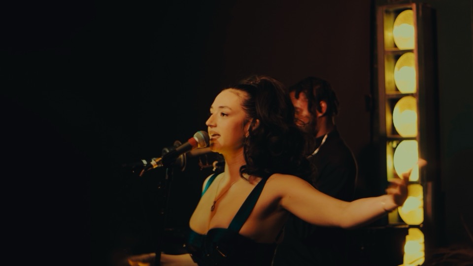 Still from Rosa Cecilia: she sings under a row of bulbs.